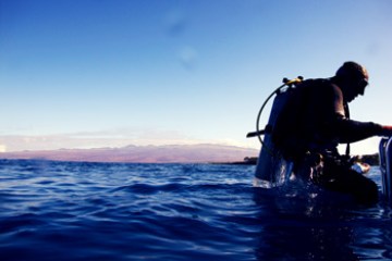 Diver sitting on the edge of boat at dusk